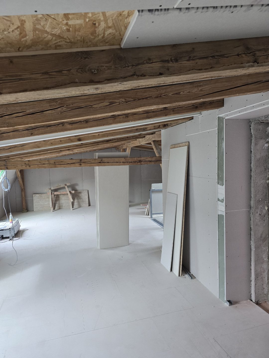 Laufender Dachgeschoss-Ausbau mit freigelegten Holzbalken und Trockenbauwänden