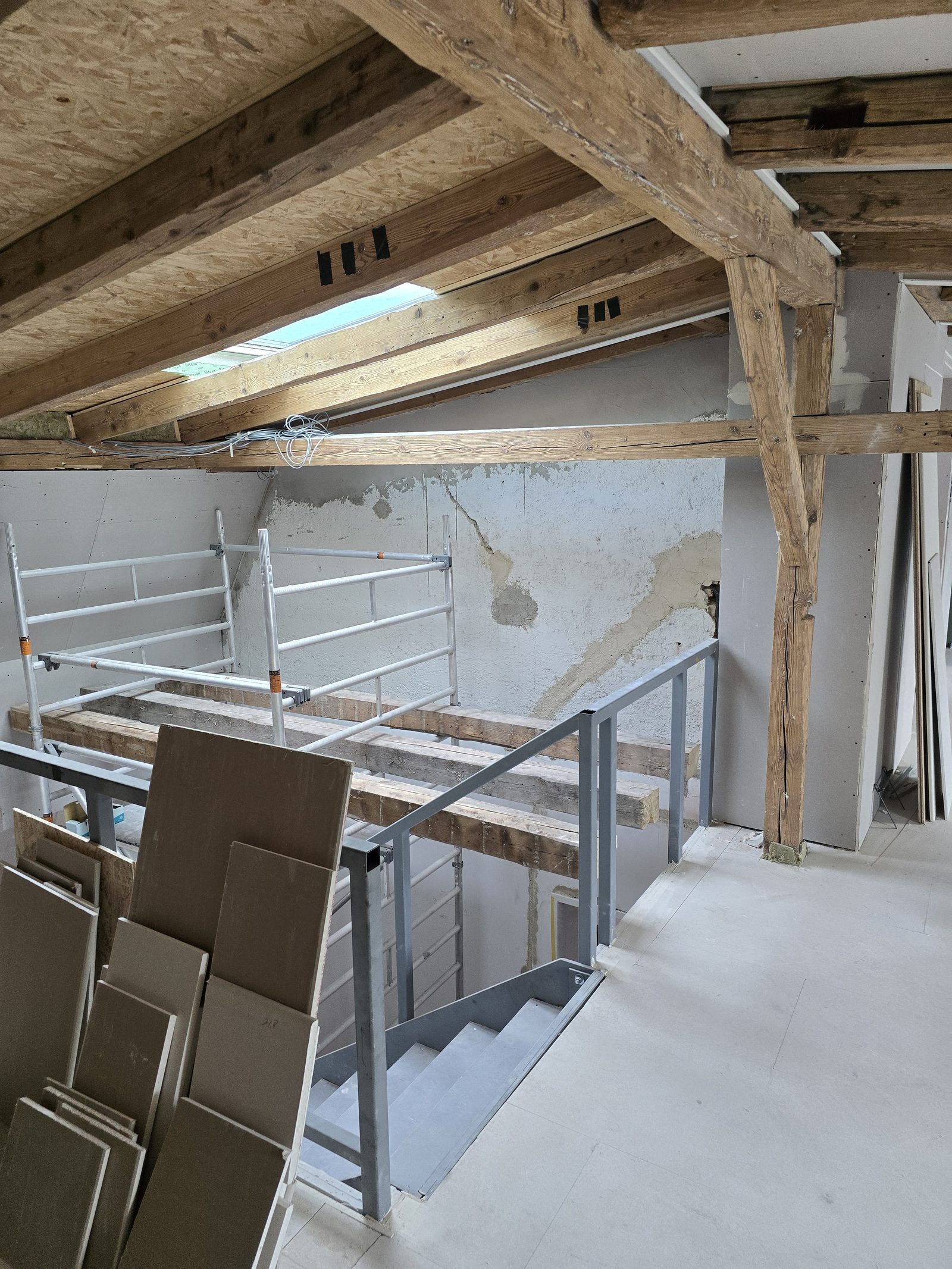 Neue Treppe mit Geländer unter freigelegten Holzbalken